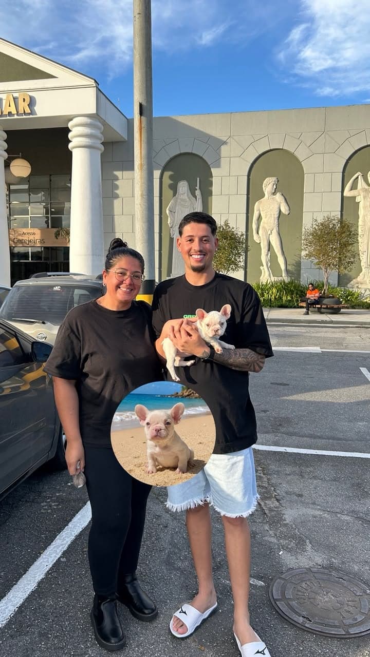 Casal sorridente segurando um filhote de Bulldog Francês claro no dia da entrega