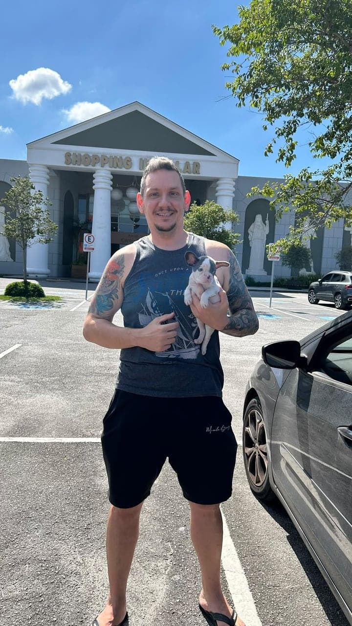 Tutor sorridente segurando um filhote de Bulldog Francês preto e branco